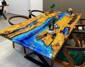 May include: A large wooden dining table with a blue and black epoxy resin river design. The table has a black metal base and is surrounded by four chairs with dark wood frames and green upholstery.