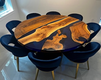 May include: A round wooden dining table with a blue epoxy resin inlay. The table is surrounded by eight blue velvet chairs with gold legs.