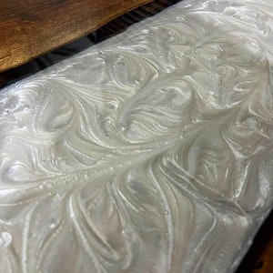 Puede incluir: Resina epoxi blanca con un patr&oacute;n de m&aacute;rmol en espiral. La resina se vierte sobre una superficie de madera.