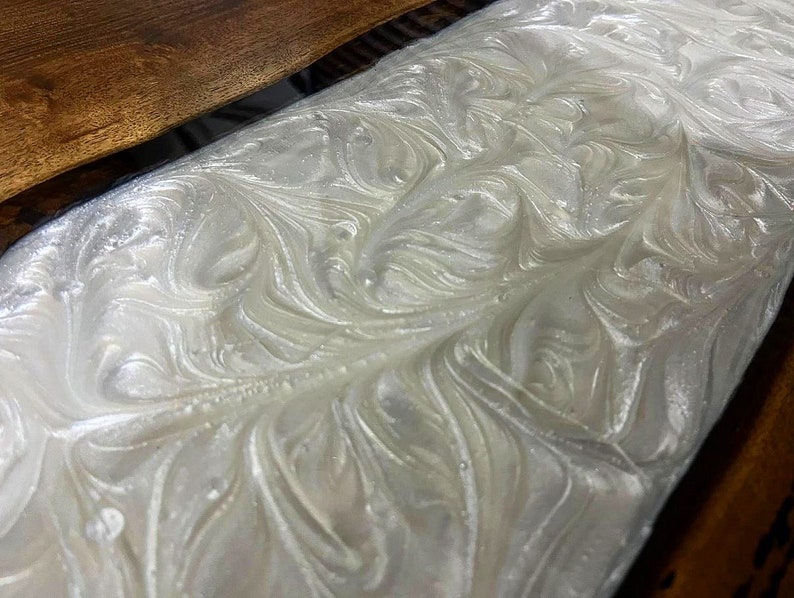 Puede incluir: Resina epoxi blanca con un patr&oacute;n de m&aacute;rmol en espiral. La resina se vierte sobre una superficie de madera.