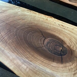 Puede incluir: Primer plano de una mesa de madera con un nudo grande en el centro. La madera es de color marr&oacute;n claro con anillos marrones m&aacute;s oscuros alrededor del nudo. El nudo est&aacute; agrietado y tiene un centro marr&oacute;n oscuro.