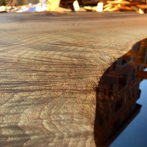 May include: Close-up of a wooden table top with a natural wood grain pattern. The edge of the table is filled with clear epoxy resin, creating a smooth, glassy surface.