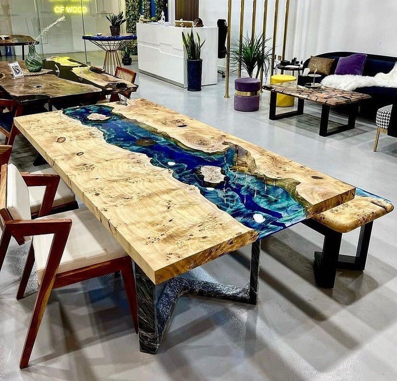 May include: A large wooden table with a blue and green epoxy resin river running through the center. The table has a black metal base and is surrounded by chairs.