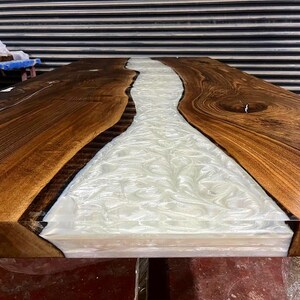 Puede incluir: Primer plano de una mesa de madera con un r&iacute;o de resina blanca que recorre el centro. La madera es de un color marr&oacute;n intenso y la resina es lisa y brillante.