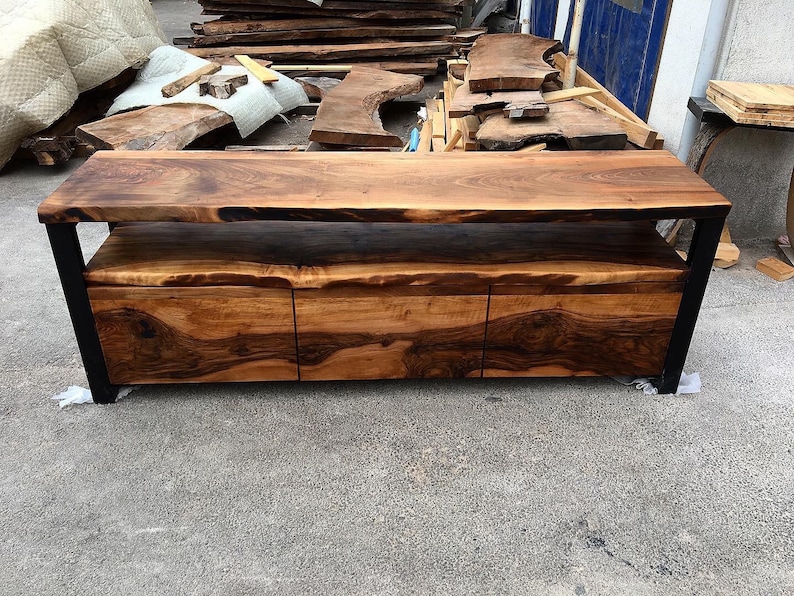 May include: A long, wooden entertainment center with a live edge top and three drawers. The center is made of dark wood with a black metal frame.