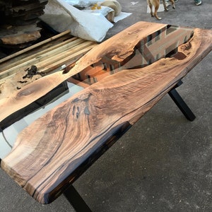 Puede incluir: Una mesa de madera con un borde vivo y un r&iacute;o de resina epoxi transparente que atraviesa el centro. La mesa tiene patas de metal negro.