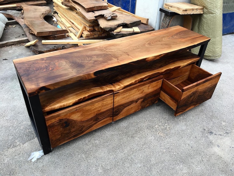 May include: A wooden entertainment center with a live edge top and three drawers. The drawers are made of wood with a dark brown finish. The entertainment center is made of metal with a black finish.