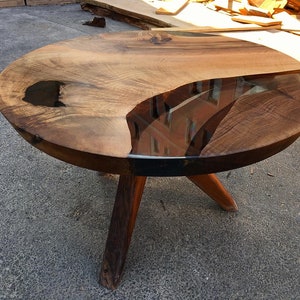 May include: A round wooden table with a unique epoxy resin design. The table has a dark brown wood top and four legs.