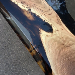 Puede incluir: Primer plano de una mesa de madera con acabado de resina epoxi negra. La veta de la madera es visible y la resina es lisa y brillante.