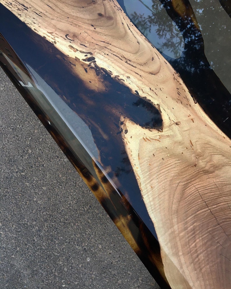 Puede incluir: Primer plano de una mesa de madera con acabado de resina epoxi negra. La veta de la madera es visible y la resina es lisa y brillante.