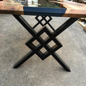 Puede incluir: Una mesa de madera con una tapa de resina epoxi negra y una base de metal negro geom&eacute;trica. La mesa tiene un acabado de madera natural.