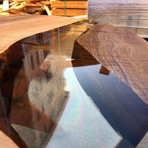 May include: Close-up of a wooden table top with a clear epoxy resin inlay. The resin is a dark blue color and has a wavy shape. The wood is a rich brown color and has a natural grain pattern.