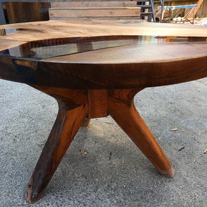 May include: A round wooden table with a unique epoxy resin inlay. The table has a dark brown wood finish and three legs.