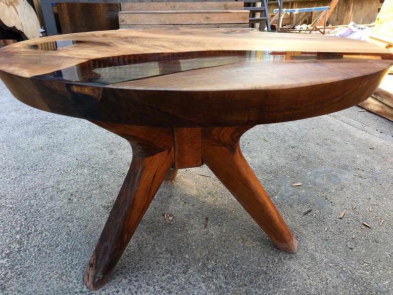 May include: A round wooden table with a unique epoxy resin inlay. The table has a dark brown wood finish and three legs.