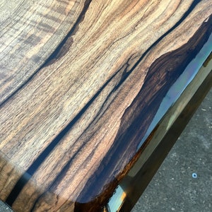 Puede incluir: Primer plano de una mesa de madera con un borde de resina epoxi marr&oacute;n oscuro. La veta de la madera es visible y tiene un aspecto natural y r&uacute;stico.
