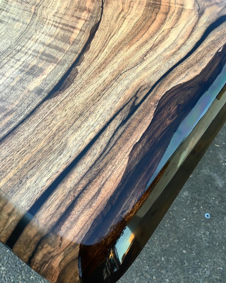 Puede incluir: Primer plano de una mesa de madera con un borde de resina epoxi marr&oacute;n oscuro. La veta de la madera es visible y tiene un aspecto natural y r&uacute;stico.