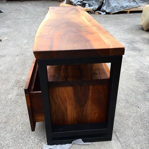 May include: A wooden TV stand with a live edge top and a black metal frame. The stand has a drawer and a shelf.