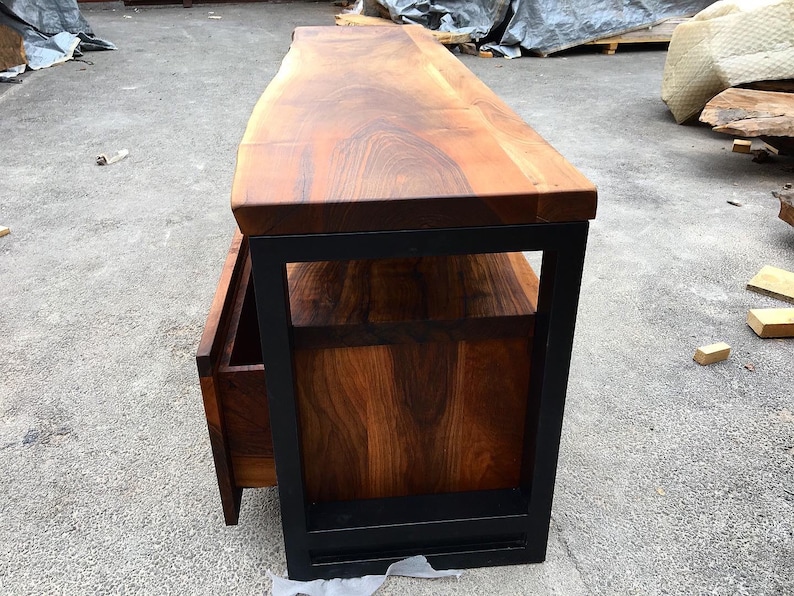 May include: A wooden TV stand with a live edge top and a black metal frame. The stand has a drawer and a shelf.