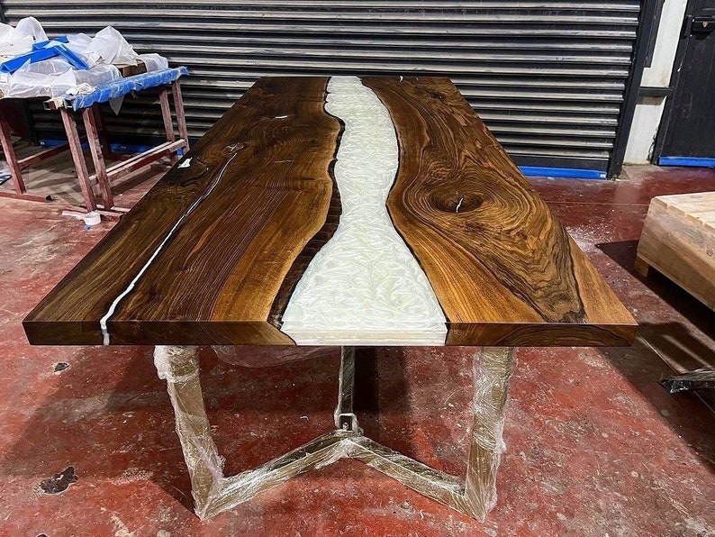 Puede incluir: Una mesa de madera grande con un r&iacute;o de resina blanca que recorre el centro. La mesa tiene un acabado de madera natural y una base de metal.