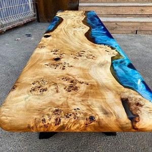 May include: A large wooden table with a blue epoxy resin inlay. The wood has a natural burl pattern and the resin is a deep blue color.