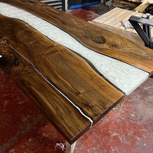 Puede incluir: Una tapa de mesa de madera marr&oacute;n oscuro con un r&iacute;o de resina blanca que recorre el centro. La tapa de mesa tiene un patr&oacute;n de veta de madera natural.