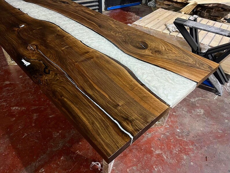 Puede incluir: Una tapa de mesa de madera marr&oacute;n oscuro con un r&iacute;o de resina blanca que recorre el centro. La tapa de mesa tiene un patr&oacute;n de veta de madera natural.