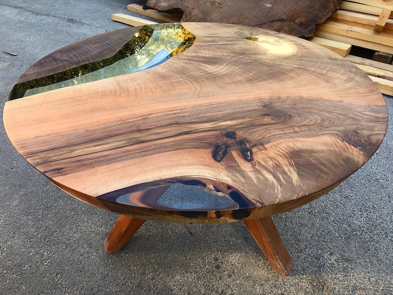 May include: Round wooden table with a live edge and a clear epoxy river running through the center. The table has three legs.