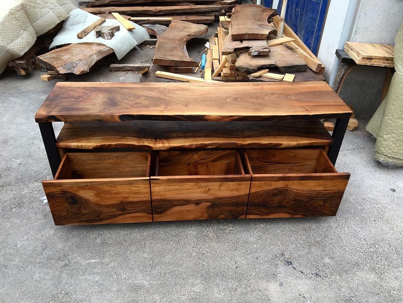 May include: A wooden entertainment center with a live edge top and three drawers. The drawers are made of wood and have a black metal frame.