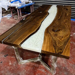 Puede incluir: Una mesa de madera grande con un r&iacute;o de epoxi blanco que atraviesa el centro. La mesa tiene una veta de madera marr&oacute;n oscura y un borde natural.