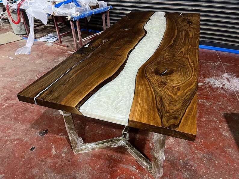 Puede incluir: Una mesa de madera grande con un r&iacute;o de epoxi blanco que atraviesa el centro. La mesa tiene una veta de madera marr&oacute;n oscura y un borde natural.