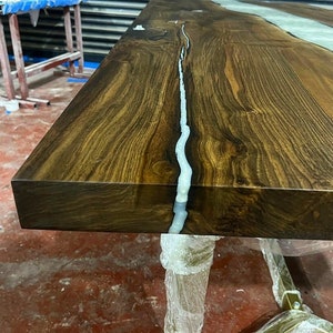 Puede incluir: Primer plano de una mesa de madera marr&oacute;n oscuro con un r&iacute;o de resina blanca que atraviesa el centro. La superficie de la mesa es lisa y pulida.