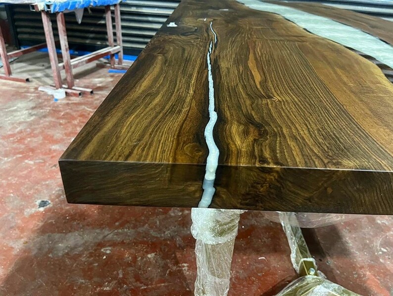 Puede incluir: Primer plano de una mesa de madera marr&oacute;n oscuro con un r&iacute;o de resina blanca que atraviesa el centro. La superficie de la mesa es lisa y pulida.