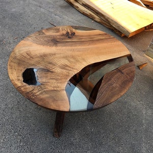 May include: A round wooden coffee table with a live edge top and epoxy resin inlay. The table has a natural wood finish and three legs.