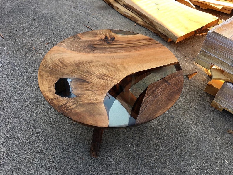 May include: A round wooden coffee table with a live edge top and epoxy resin inlay. The table has a natural wood finish and three legs.