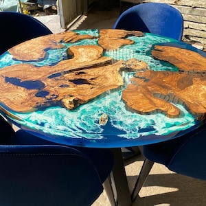 Könnte beinhalten: Ein runder Holztisch mit einer blauen und weißen Epoxidharzplatte. Der Tisch ist von vier blauen Samt-Stühlen umgeben.