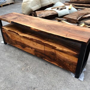 May include: A long, dark wood console table with a live edge top and three drawers. The table has a black metal frame and a shelf below the top.