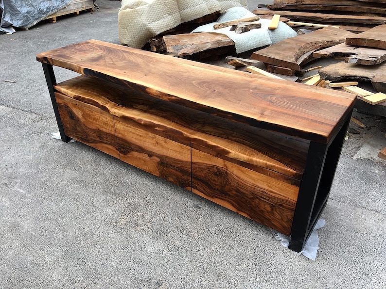 May include: A long, dark wood console table with a live edge top and three drawers. The table has a black metal frame and a shelf below the top.