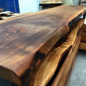 May include: A dark brown live edge wood console table with two drawers. The table top has a natural, live edge finish and the drawers are made of a lighter wood.