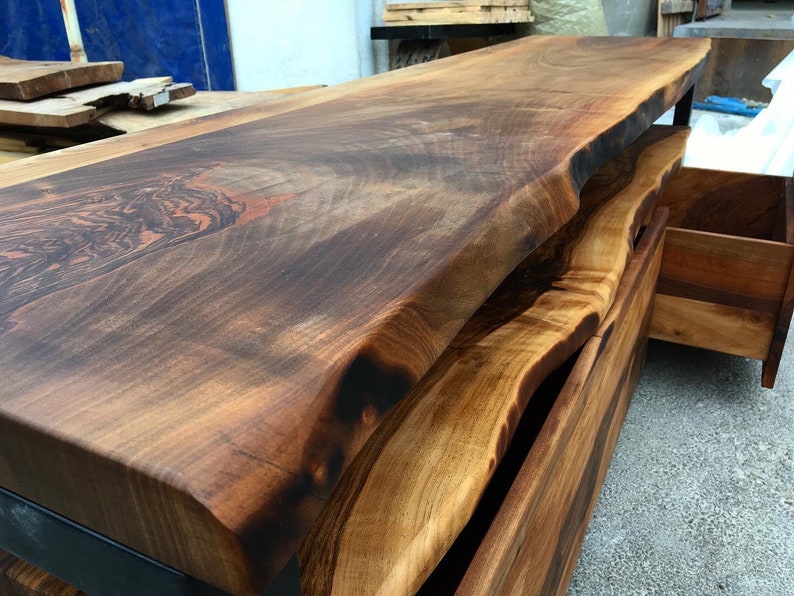 May include: A dark brown live edge wood console table with two drawers. The table top has a natural, live edge finish and the drawers are made of a lighter wood.