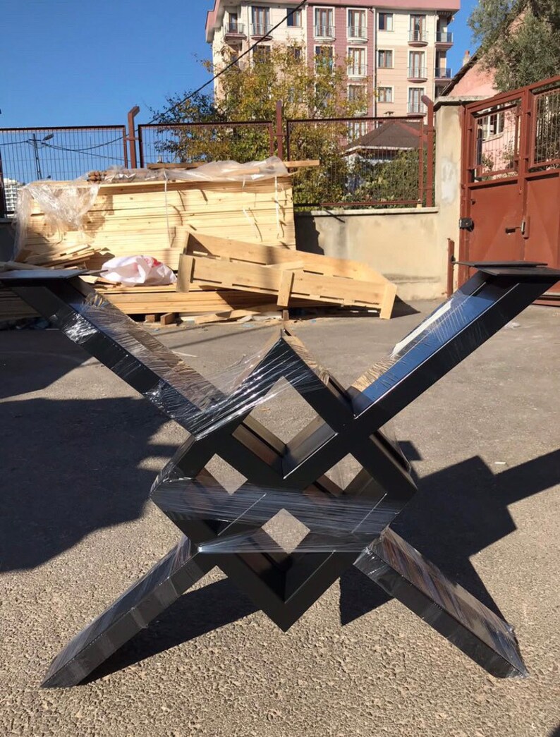 Puede incluir: Base de mesa de metal negro con un dise&ntilde;o geom&eacute;trico. La base est&aacute; hecha de cuatro piezas de metal que se cruzan para formar una forma cuadrada. La base est&aacute; envuelta en pl&aacute;stico.