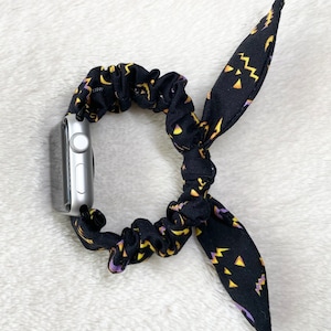 May include: Black and yellow patterned fabric watch band with a bow. The band is made of a stretchy material and is designed to fit a smartwatch.