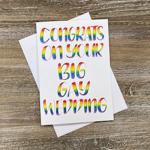 May include: A white card with the text "Congrats on your big gay wedding" written in rainbow colours.