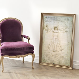 Może przedstawiać: Fotel obity purpurowym aksamitem z ozdobną, pozłacaną ramą z drewna stoi przed obrazem Leonarda da Vinci przedstawiającym Człowieka Witruwiańskiego.