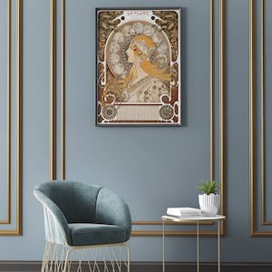 May include: A framed art print of a woman with long flowing hair, surrounded by intricate floral and geometric designs. The print is titled "La Plume" and features a calendar with the months of the year.