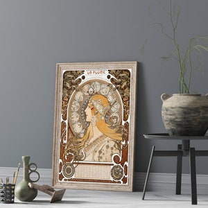 May include: A vintage poster featuring a woman with long flowing hair, surrounded by a decorative floral design. The poster is titled "La Plume" and is framed in a light wood frame.
