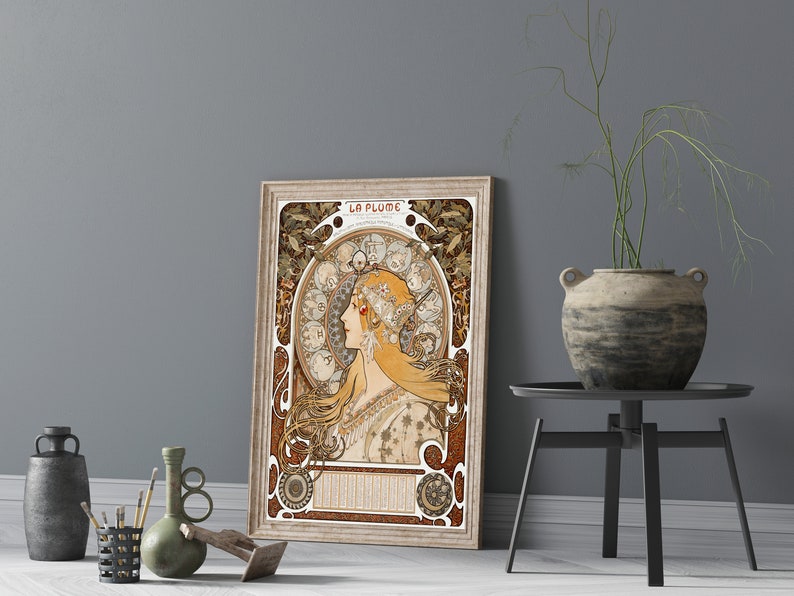May include: A vintage poster featuring a woman with long flowing hair, surrounded by a decorative floral design. The poster is titled "La Plume" and is framed in a light wood frame.