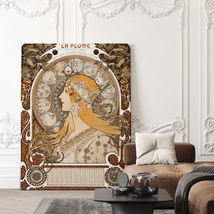 May include: A vintage art nouveau poster featuring a woman with flowing hair and a crown of flowers. The poster is titled "La Plume" and features a circular design with zodiac symbols. The poster is printed on a textured paper and has a brown and gold color scheme.