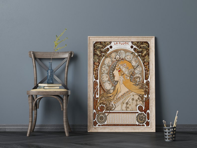 May include: A vintage art nouveau poster featuring a woman with long flowing hair, surrounded by a circular design of zodiac symbols. The poster is framed in a light wood frame and has the title "LA PLUME" at the top.