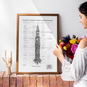 May include: A black and white diagram of the Saturn V Apollo flight configuration, showing the different stages of the rocket. The diagram is framed in a brown wooden frame and is hanging on a white wall.