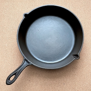 May include: A black cast iron skillet with a smooth, dark surface. The skillet has a long handle and a rounded shape.